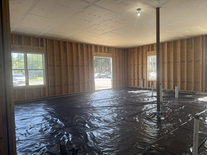 Interior corner with vapor barrier on the floor, framed walls, a capped stub-up marked SINK, and an open door frame looking out to the parking lot.