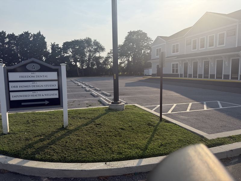 Parking lot in front of the Plantations Professional Park building at golden hour, with marked spaces, wheel stops, a lamp post, and the building directory sign at the left.